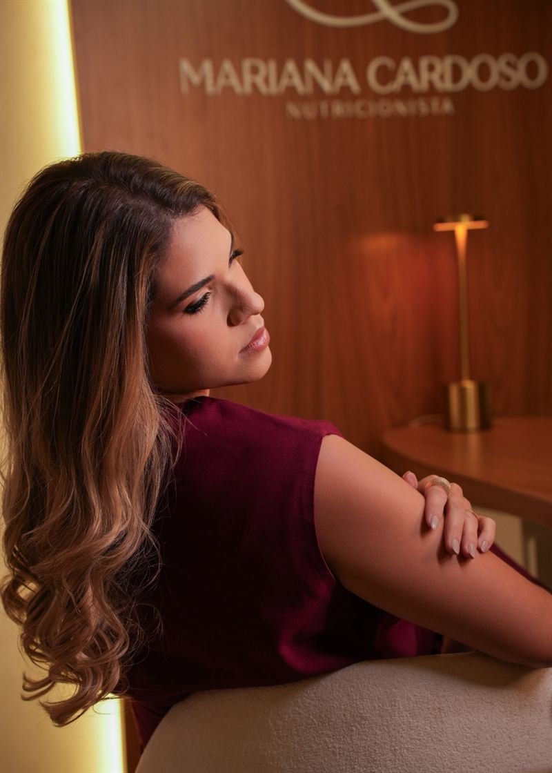 Mariana Cardoso no consultório, com o logotipo da marca ao fundo
